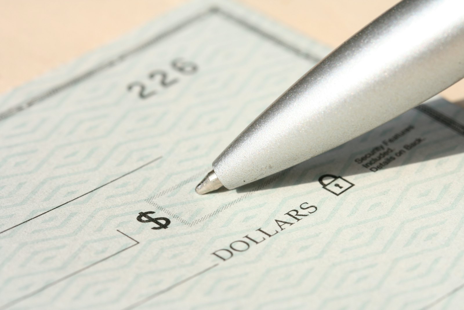 A silver pen resting over the dollar amount box of a blank paper check.